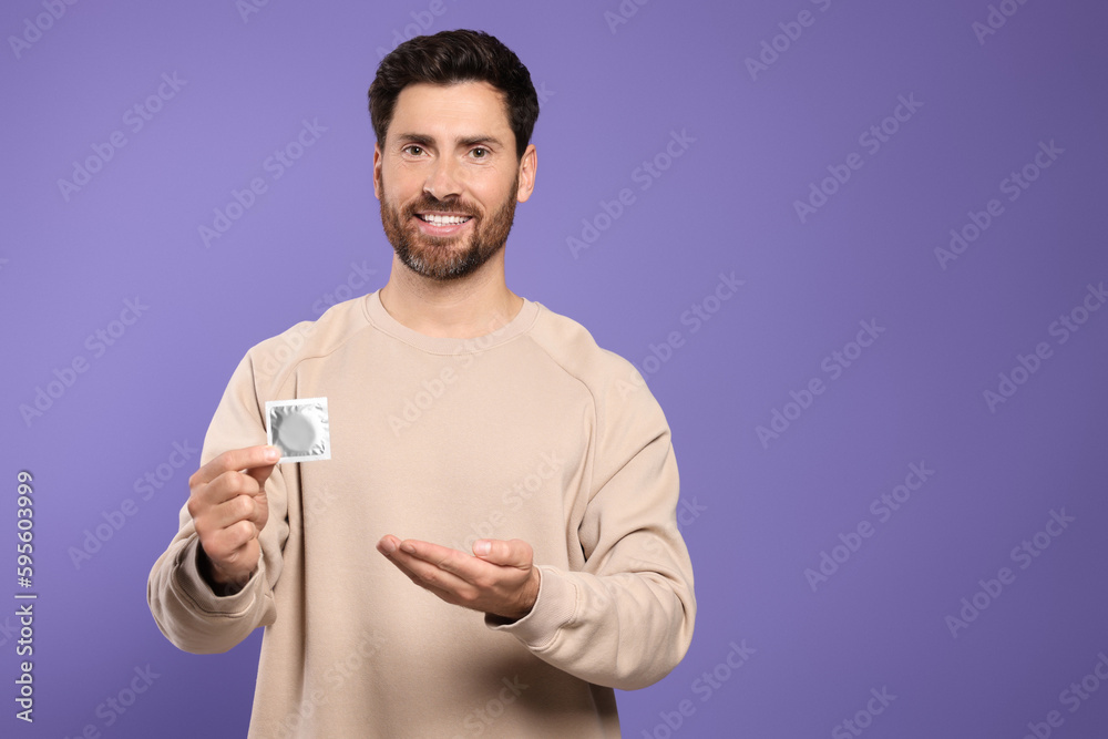 Man holding condom on purple background, space for text. Safe sex Man holding condom on purple background, space for text. Safe sex
