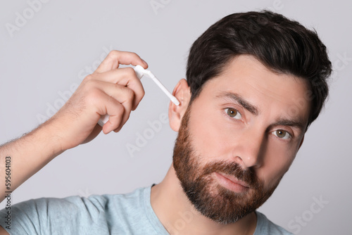 Man using ear spray on grey background