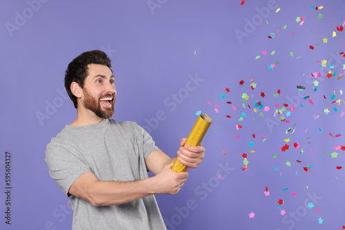 Quadro su tela Emotional man blowing up party popper on violet background