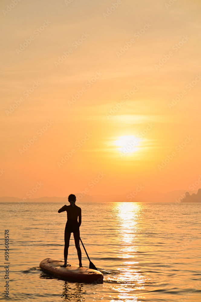 A woman paddling a supboard in the sea at sunset.