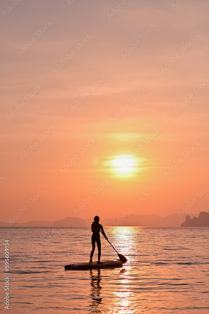 A woman paddling a supboard in the sea at sunset.