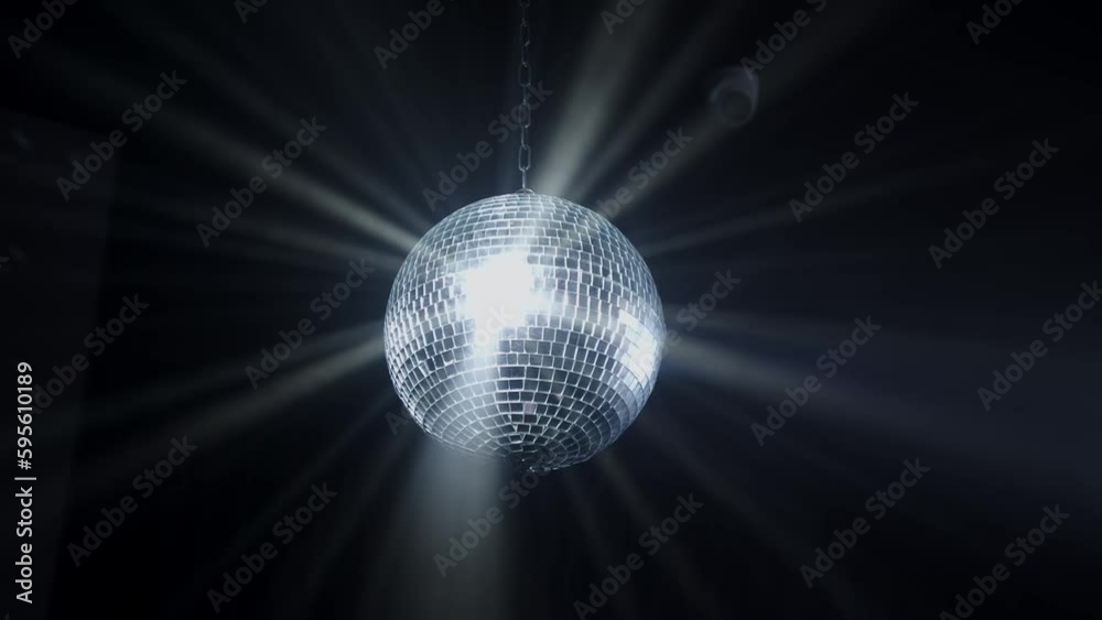 Disco Ball with Reflected Moving Rays Rotating. Mirror disco ball in white light. Isolated disco ball on black background. Close-up. Mirror ball spinning indoors. Performance. The reflection of lights