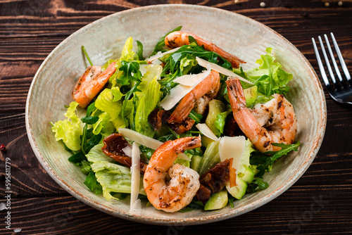 Salad of shrimp, avocado, sun-dried tomatoes, parmesan cheese, lettuce and arugula in plate.