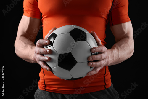 Athletic man with soccer ball on black background, closeup