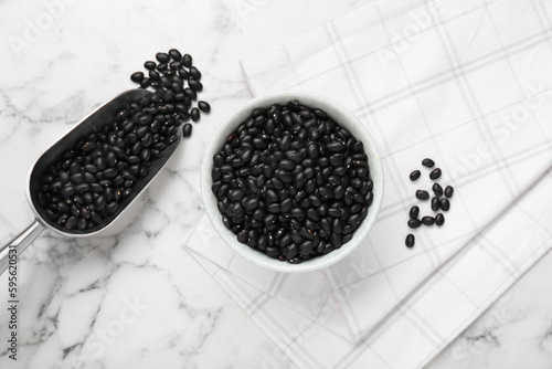 Bowl and scoop of raw black beans on white marble table, flat lay