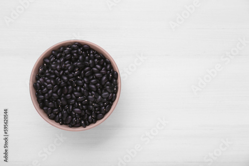 Bowl of raw black beans on white wooden table, top view. Space for text
