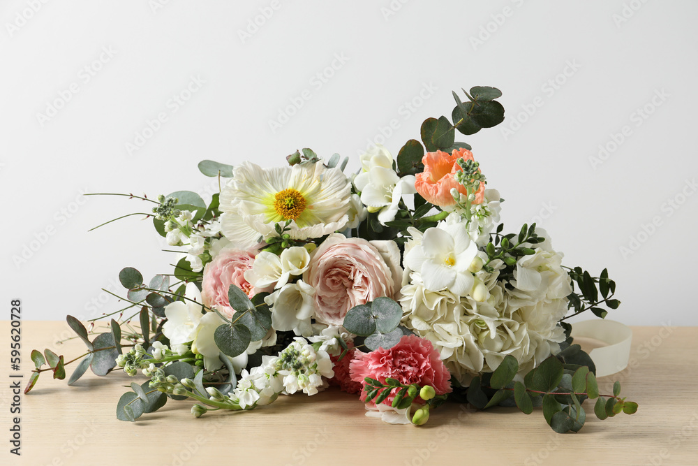 Bouquet of beautiful flowers on wooden table against white wall Bouquet of beautiful flowers on wooden table against white wall