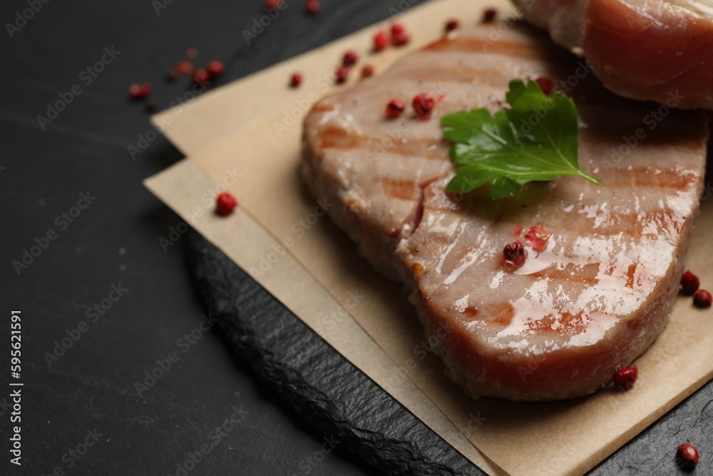 Delicious tuna steak with parsley and spices on black table, closeup. Space for text
