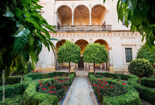 16th-century tiled gardens in the Casa de Pilatos palace with green plants and red flowers. Renaissance architecture style arches. Sevilla, Andalusia, Spain. © Soloviova Liudmyla