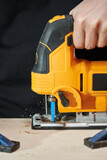 laser-illuminated electric jigsaw sawing a fixed wooden board close-up