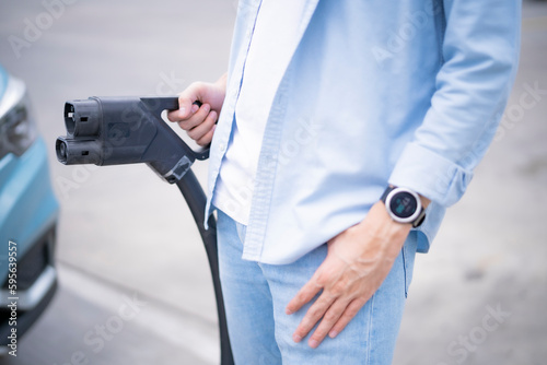 Close up of man hand holding electrical car cable charger ready for fill energy to his electric car, using eco energy concept.