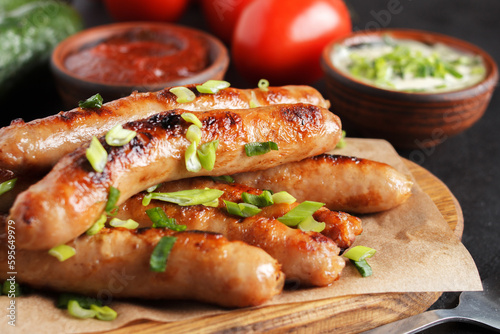 Delicious sausages on a wooden board with various sauces and fresh vegetables on a wooden table. c
