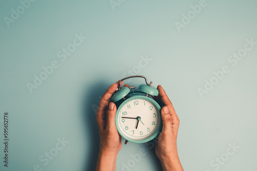 Fototapeta Naklejka Na Ścianę i Meble -  Hand holding an alarm clock on blue background