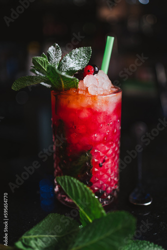 Shot of a berries mojito on a bar counter. It is surrounded by mint leaves.