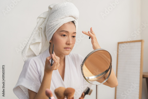 Canvas Print Happy beauty blogger concept, beautiful asian young woman, girl in bathrobe makeup face by applying black eyeliner, hand in putting on eye looking at the mirror