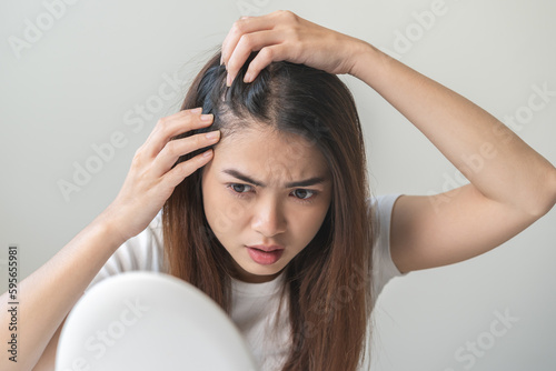 Damaged Hair symptom, face serious asian young woman, girl worry about balding, looking at scalp in mirror, hand in break into front hair loss, thin problem. Health care treatment for beauty concept.