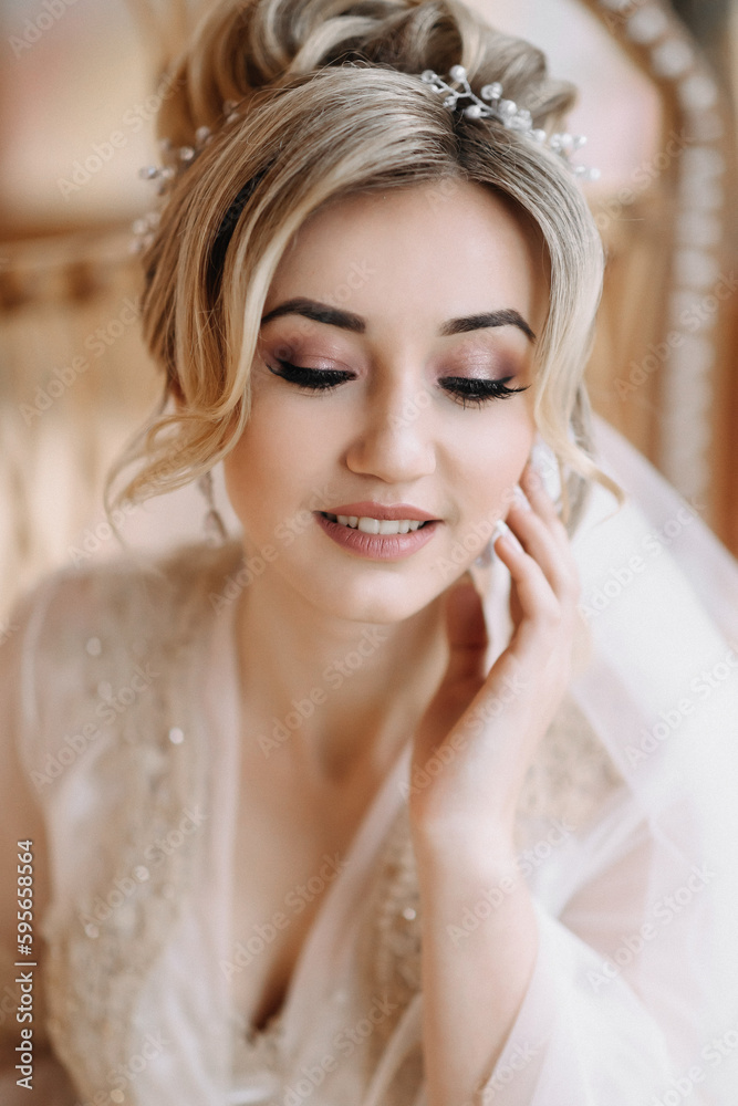 Blonde bride with elegant hairdo and tiara, wearing a robe, posing, looking at the camera, touching her face. Beautiful makeup. Elegant hairstyle. French manicure