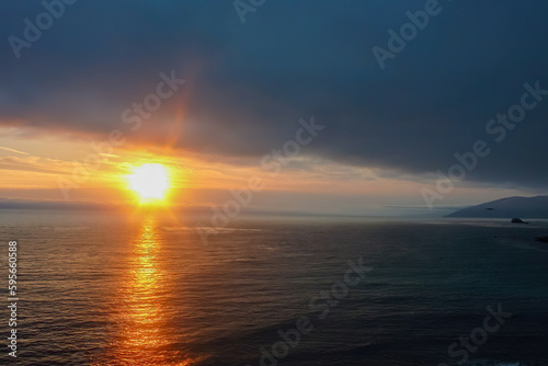 Watching sunset from Bixby Creek Bridge on coastline of Big Sur, Monterey county, California, USA, America. View of horizon of Pacific Ocean. Sun is reflecting in calm sea. Vibrant clouds in the sky © Chris