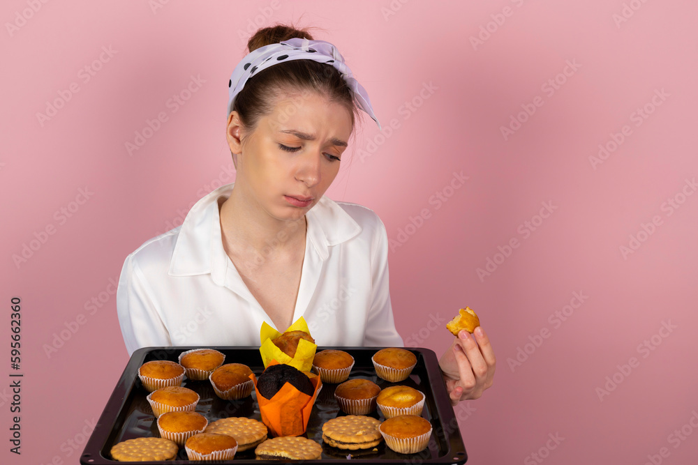 Cute sad girl eats muffins and pastries and looking with sadness at the bitten piece. Isolated on pink background. Cute sad girl eats muffins and pastries and looking with sadness at the bitten piece. Isolated on pink background.