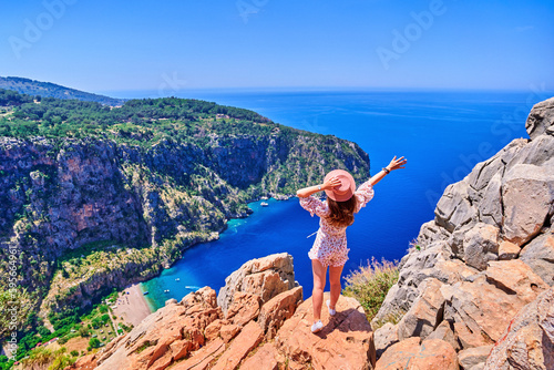 Free carefree girl traveler with open arms stands on hill rock over blue sea bay in Turkey, butterfly valley