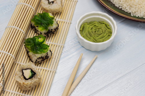 Seaweed sushi set on bamboo sushi mat. Wasabi in a bowl. Chopsticks on the table.