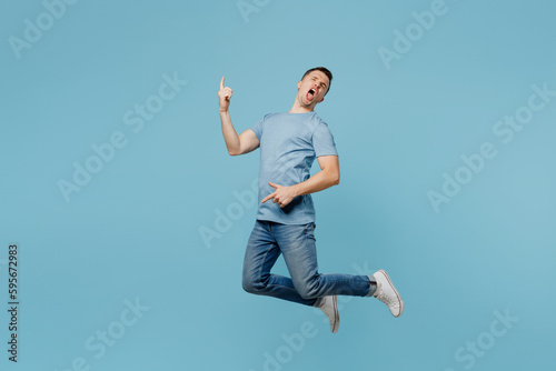 Full body young smiling happy cheerful man wear casual t-shirt jump high pretend play guitar with hands gesture isolated on plain pastel light blue cyan background studio portrait. Lifestyle concept.