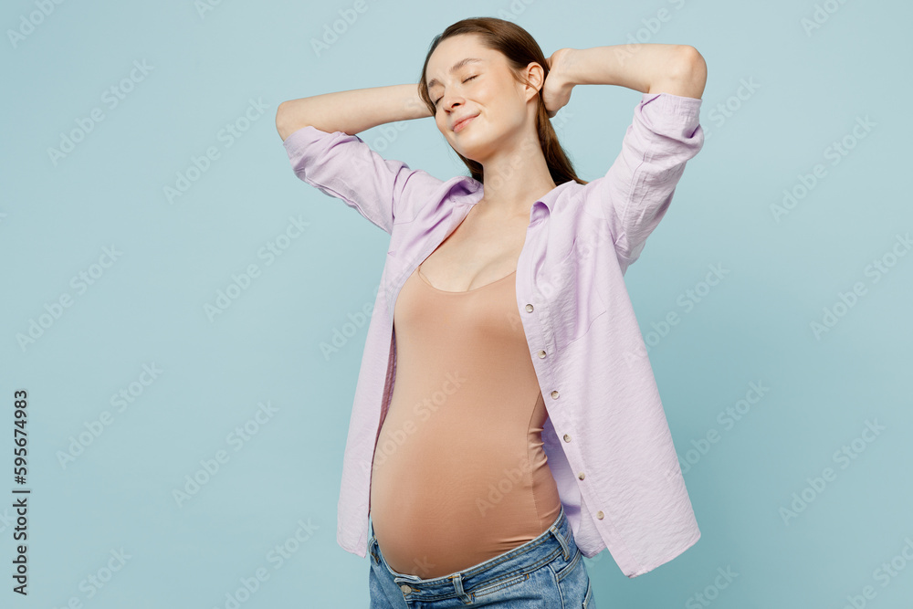 Fototapeta premium Young happy fun pregnant future mom woman with belly tummy with baby wear casual clothes hold hands behind neck close eyes rest isolated on plain pastel blue background. Maternity pregnancy concept.