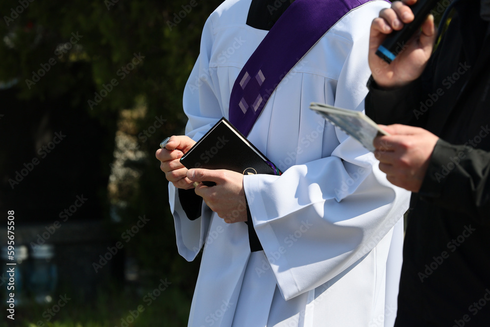 Ksiądz katolicki w komży z fioletowa stułą podczas celebracji pogrzebu.  - obrazy, fototapety, plakaty 