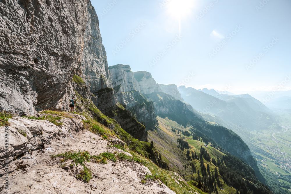 Sporty woman enjoys amazing view on the Churfürsten mountain range from hike trail below steep rock wall. Schnürliweg, Walensee, St. Gallen, Switzerland, Europe.