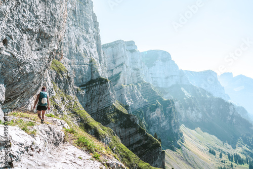 A sportive woman walks on hike trail below steep rock wall with amazing view on the Churfürsten mountain range. Schnürliweg, Walensee, St. Gallen, Switzerland, Europe.