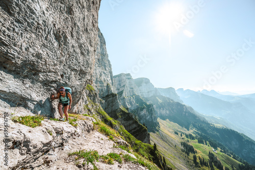 Young woman walks on hike trail below steep rock wall with amazing view on the Churfürsten mountain range. Schnürliweg, Walensee, St. Gallen, Switzerland, Europe.