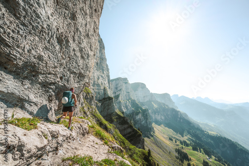An athletic woman walks on hike trail below steep rock wall with amazing view on the Churfürsten mountain range. Schnürliweg, Walensee, St. Gallen, Switzerland, Europe.