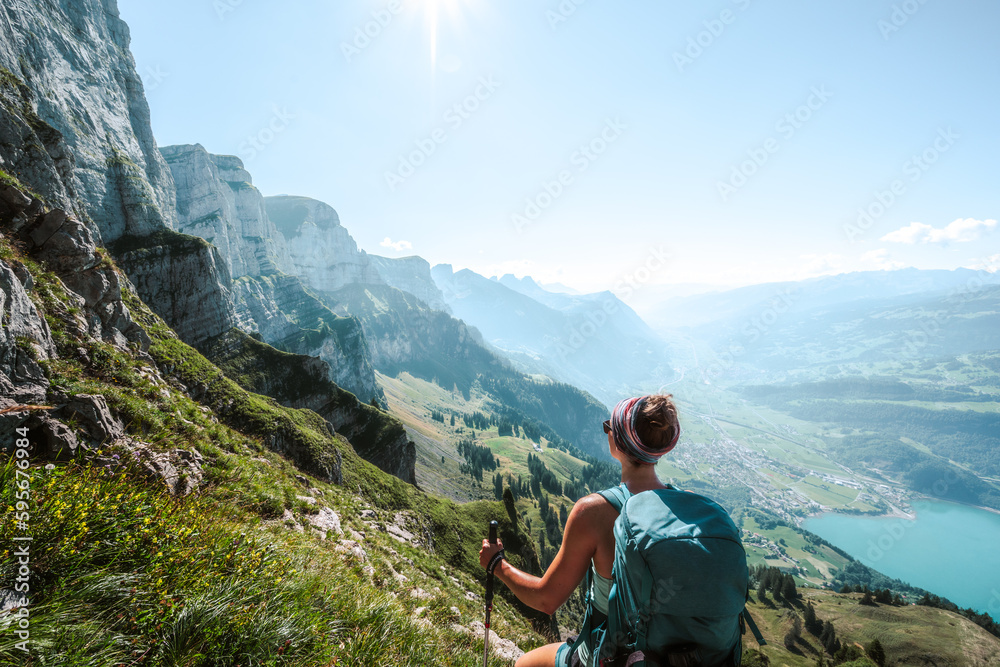 Athletic woman enjoys scenic view on the Churfürsten mountain range from hike trail below steep rock wall. Schnürliweg, Walensee, St. Gallen, Switzerland, Europe. - obrazy, fototapety, plakaty 