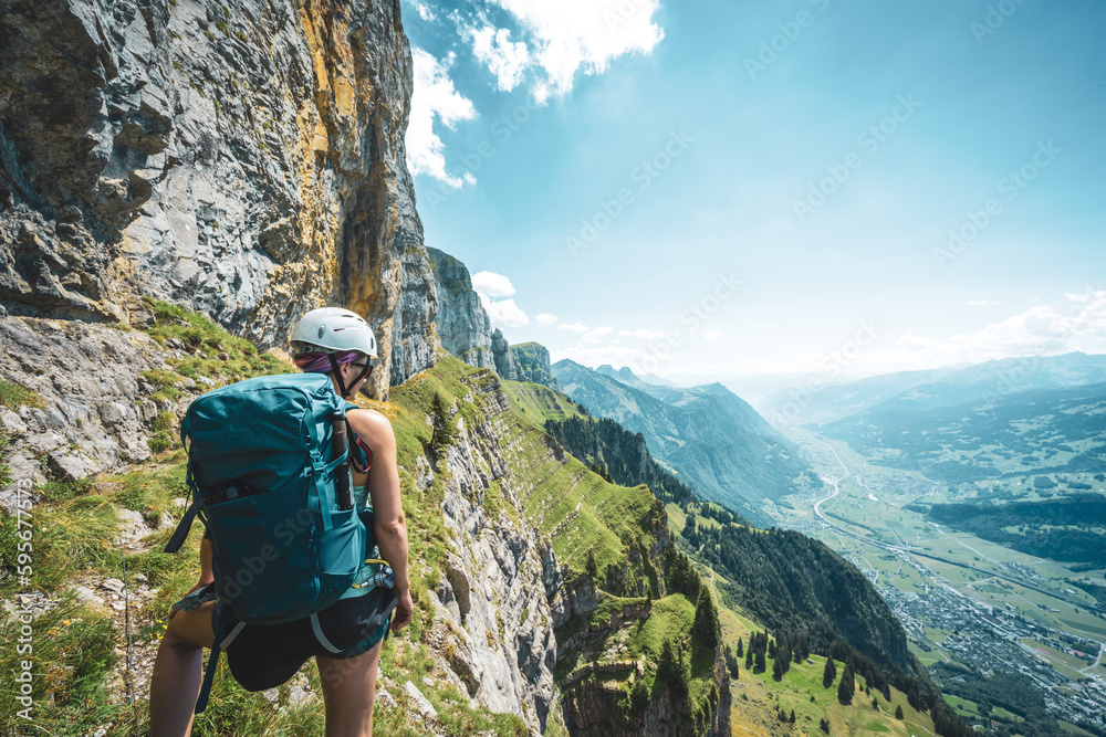 Naklejka premium Young woman on steep rocky hike trail enjoys scenic view on Churfürsten mountain range at noon. Schnürliweg, Walensee, St. Gallen, Switzerland, Europe.