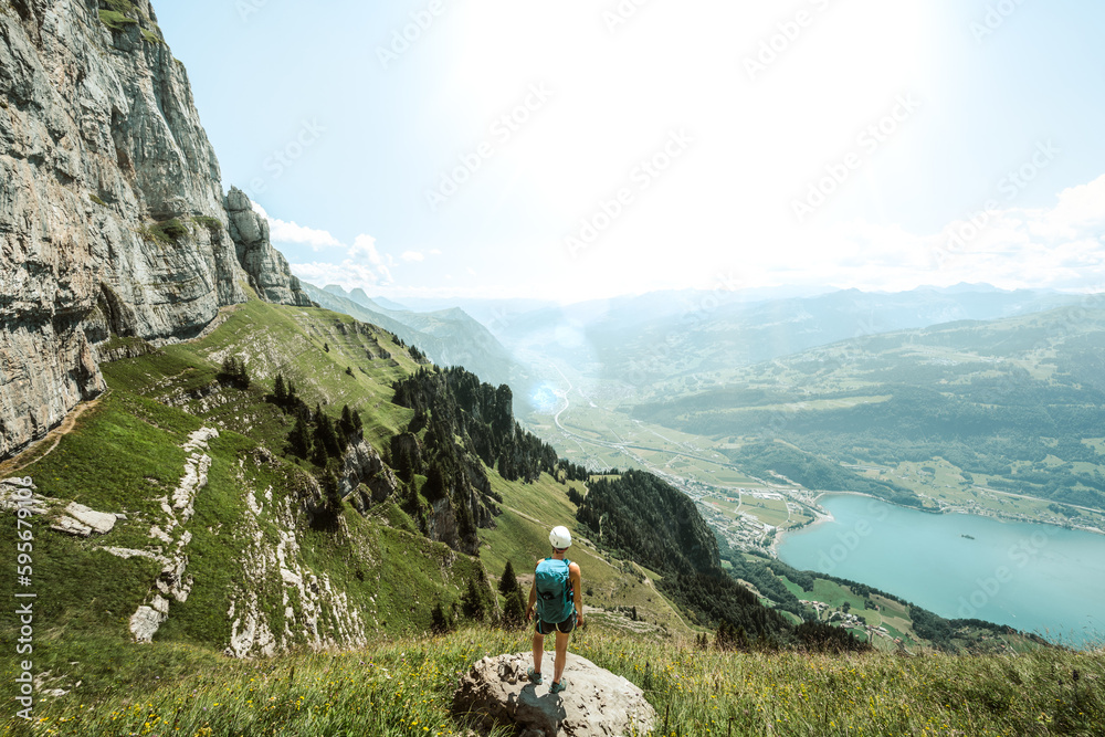 Mountaineer stands on a rock next to the hiking trail and enjoys the view of lake Walensee and Walenstadt.  Schnürliweg, Walensee, St. Gallen, Switzerland, Europe.