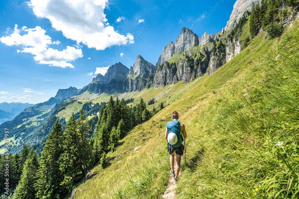 Sporty woman walks on scenic hiking trail between meadow and trees and the Churfürsten mountain range in the background. Schnürliweg, Walensee, St. Gallen, Switzerland, Europe.
