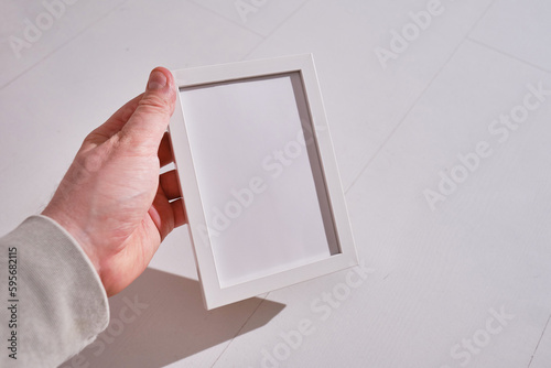 Empty white frame for text close-up in hands on a light background. Place for inscriptions and advertising. Stylish piece of furniture