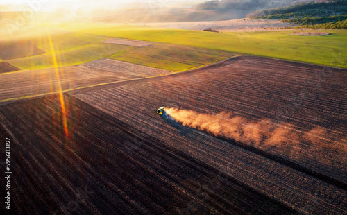 A cloud of dust rises behind a tractor plowing the ground.