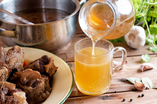 Glass jar with yellow fresh bone broth o on wooden table. Healthy low-calories food is rich in vitamins, collagen and anti-inflammatory amino acids