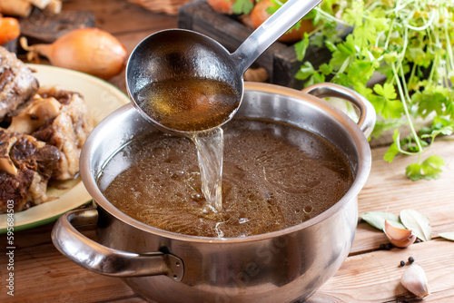 Saucepan with bouillon with a ladle on wooden table. Bone broth photo