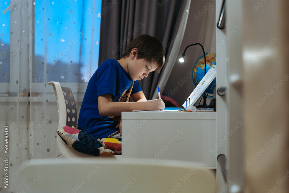 caucasian boy doing homework at home at the desk by the window. caucasian boy doing homework at home at the desk by the window.