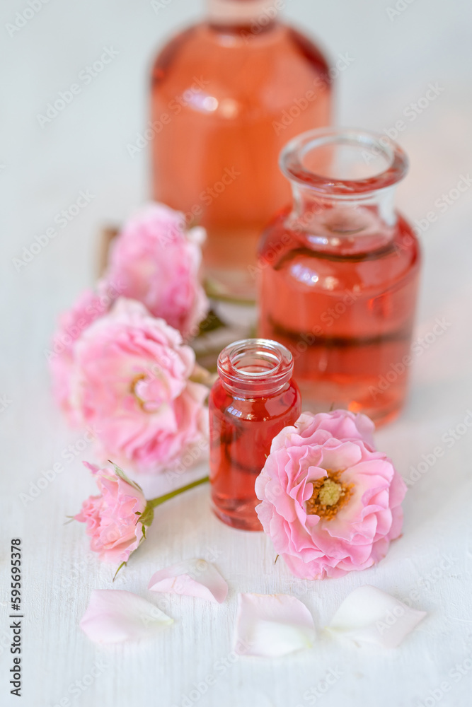 Composition with pure natural organic rose essential oil in glass bottle, luxury perfumery ingredient for premium fragrance, skin care products, anti-age beauty treatment. Fresh flowers