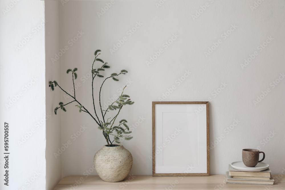 Breakfast still life. Modern living room. Cup of coffee, books. Empty wooden picture frame mockup on desk, table. Vase with green willow tree branches. Elegant Scandi working space, home office. Breakfast still life. Modern living room. Cup of coffee, books. Empty wooden picture frame mockup on desk, table. Vase with green willow tree branches. Elegant Scandi working space, home office.