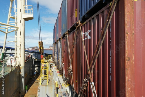 View on row of lashed containers with bars, turnbuckles and twist locks from forward of container vessel with cranes. Behind is Paranaguá the second largest port of Brazil. 