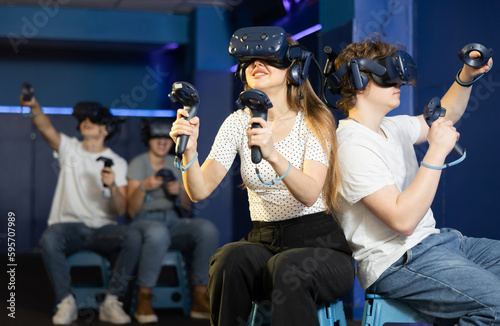 Male and female friend in helmets and with joysticks are sitting playing 3d action game. Metaverse console, entertainment club
