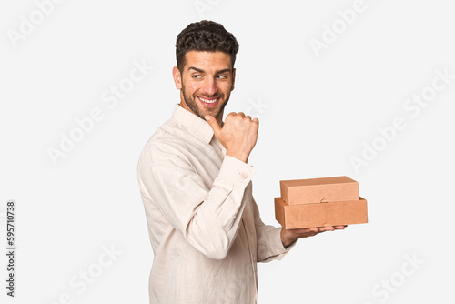 Young man holding a takeaway boxes isolated points with thumb finger away, laughing and carefree.
