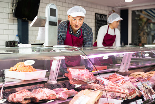 Smiling male butcher offering to sell big piece of beef in butcher shop