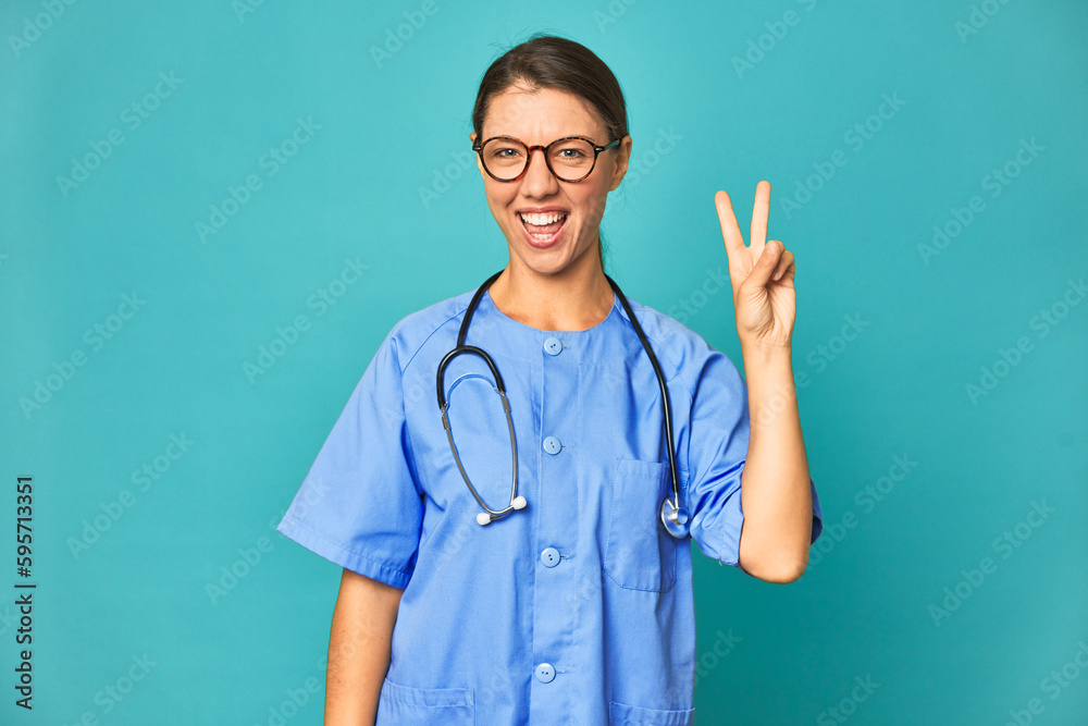 A young nurse woman isolated joyful and carefree showing a peace symbol with fingers. A young nurse woman isolated joyful and carefree showing a peace symbol with fingers.