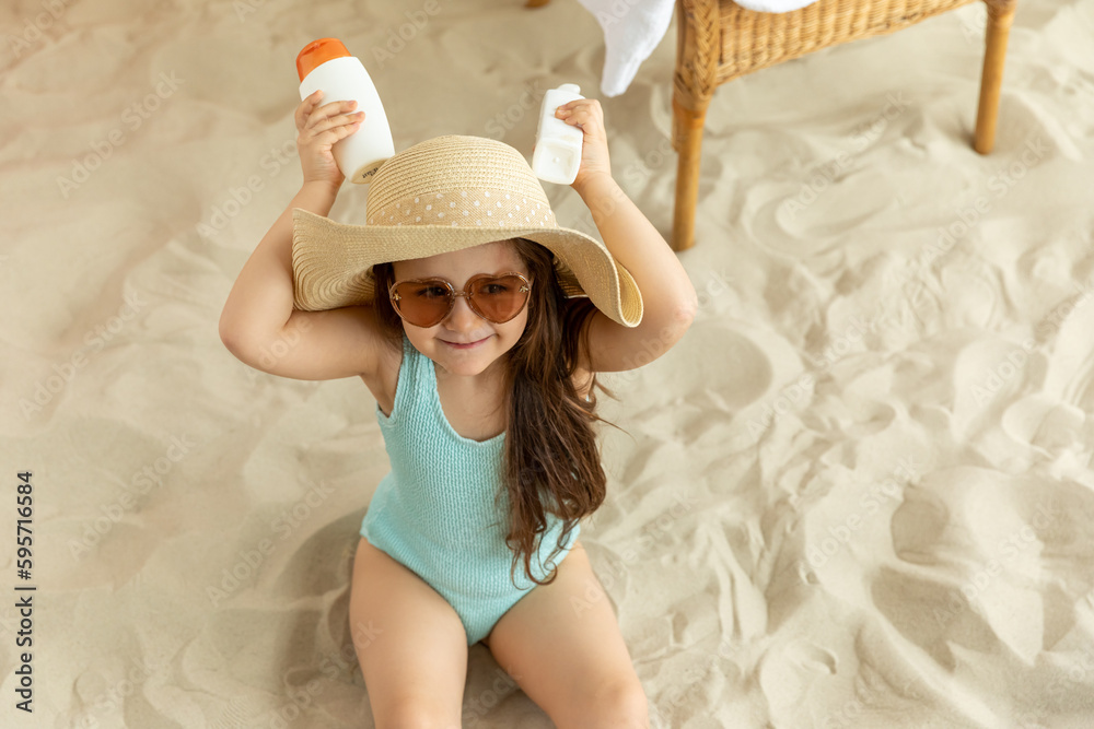 Skin care. Protection from the sun. Sunscreen for children. The Girl in a swimsuit and a straw hat is Holding a Moisturizing Sunscreen in her Hands.