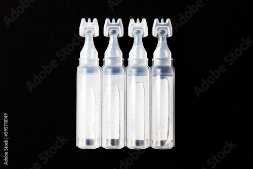 Eye drops background. Saline water capsules. Vials of saline background. Pharmacy product isolated on black. Small plastic medical bottle.